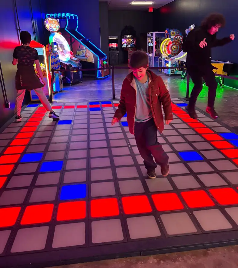 A commercial grade pressure-sensitive LED interactive game floor, showing glowing grid patterns similar to Activate Game rooms, installed in an entertainment venue