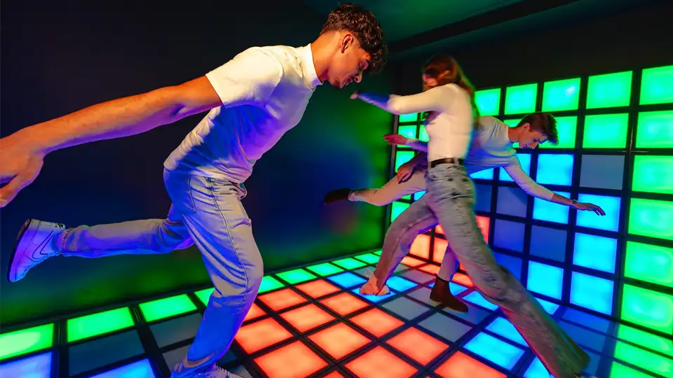 Players competing on an interactive LED game floor with glowing tiles in a commercial entertainment center.