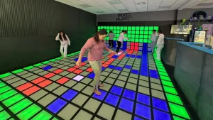 Multiple players stepping on red green and blue LED floor tiles inside a real active gaming room installation showing commercial venue scale for FEC operators