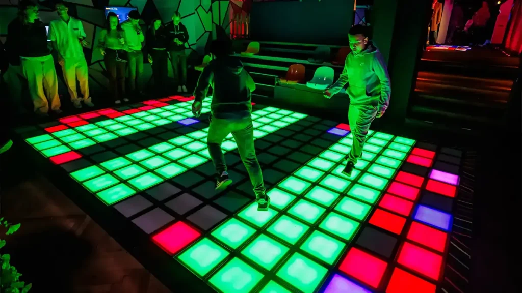Active Gaming Room vs Activate Games Franchise: What FEC Operators Should Know (2026) 3 Two players competing on colorful LED grid floor tiles inside a commercial active gaming room with spectators watching in background
