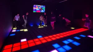 Players competing on colorful LED pixel floor game tiles inside a commercial FEC active gaming venue