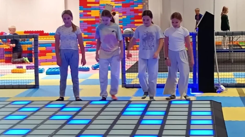 Interactive Game Floor for Indoor Playgrounds: Is It Right? 2 Older children playing an interactive game floor for indoor playgrounds while younger kids use soft play nearby